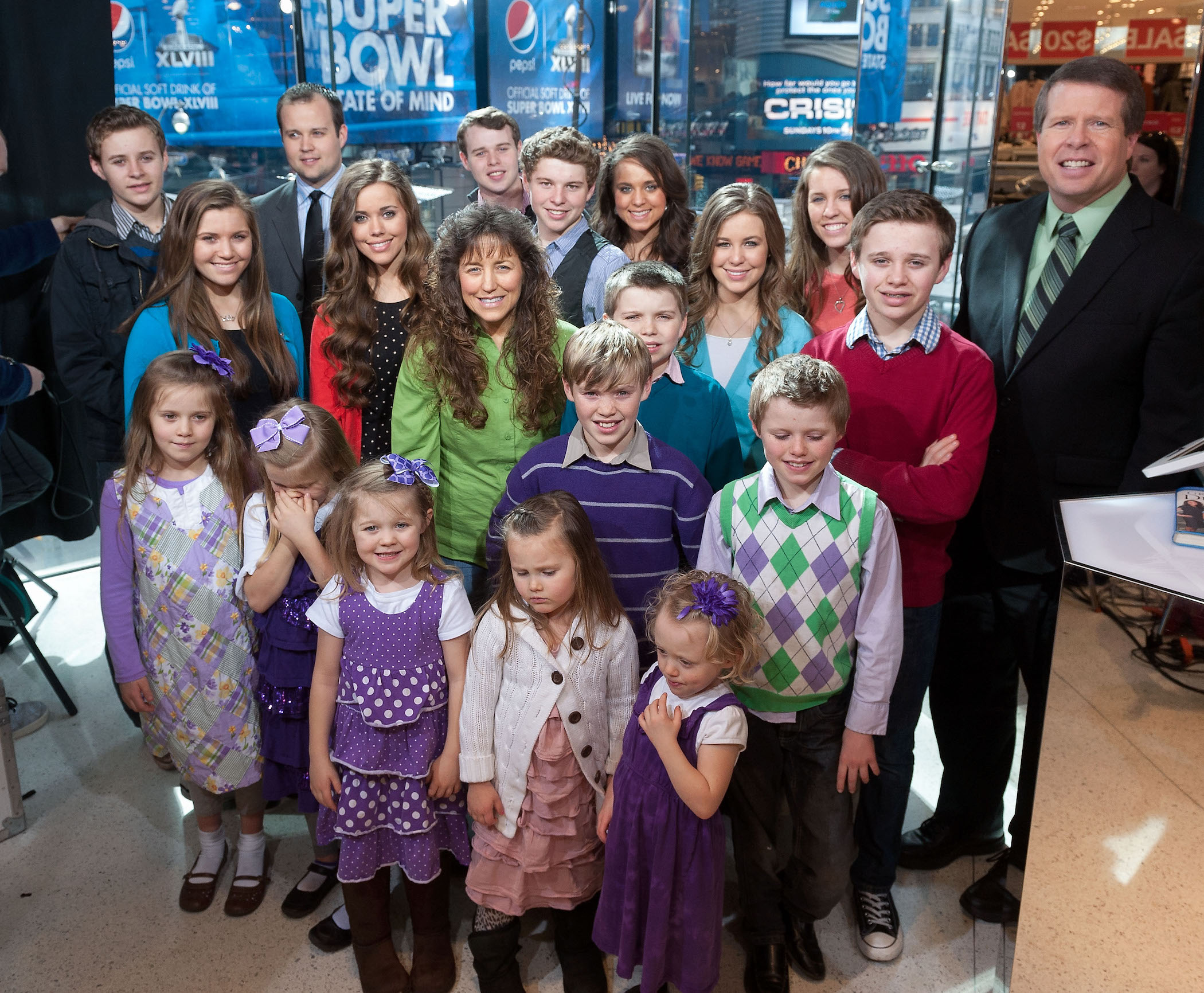 The Duggar family crowded together on stage smiling at the camera above them