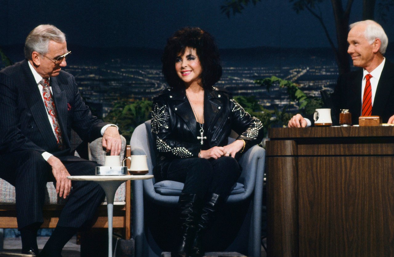 Ed McMahon in a suit, Elizabeth Taylor in black, and Johnny Carson in a black suit and red tie