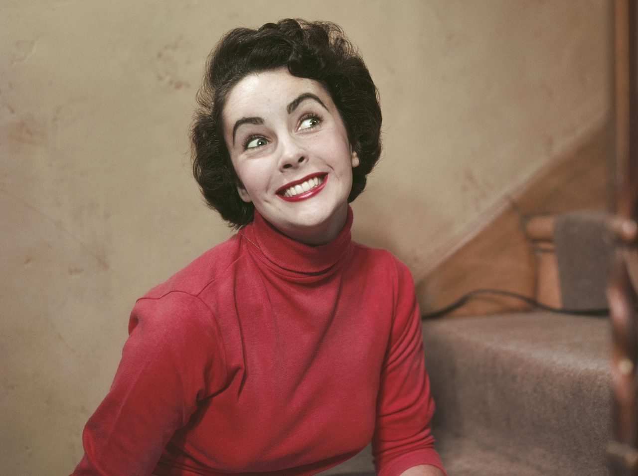 Elizabeth Taylor seated on stairs, dressed in red and smiling 