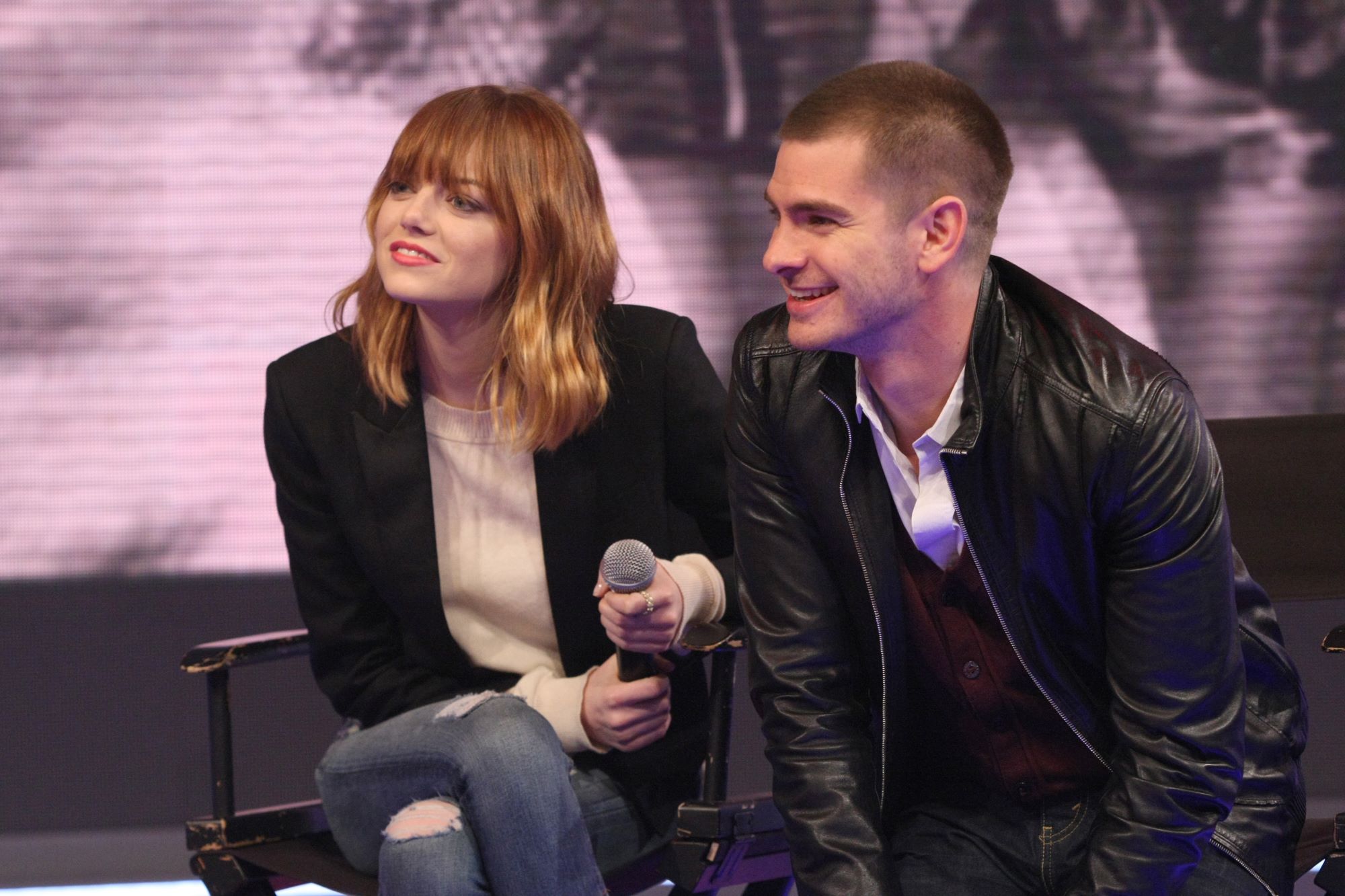 'Spider-Man: No Way Home' actor Andrew Garfield and actor Emma Stone speak onstage during a panel. Garfield wears a black leather jacket and jeans. Stone wears a black jacket over a tan sweater and jeans.