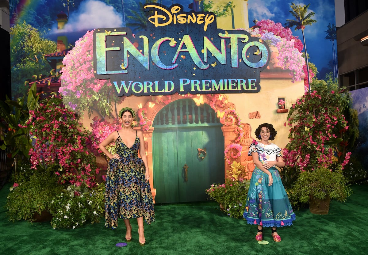 Stephanie Beatriz and Mirabel pose in front of the ‘Encanto’ logo