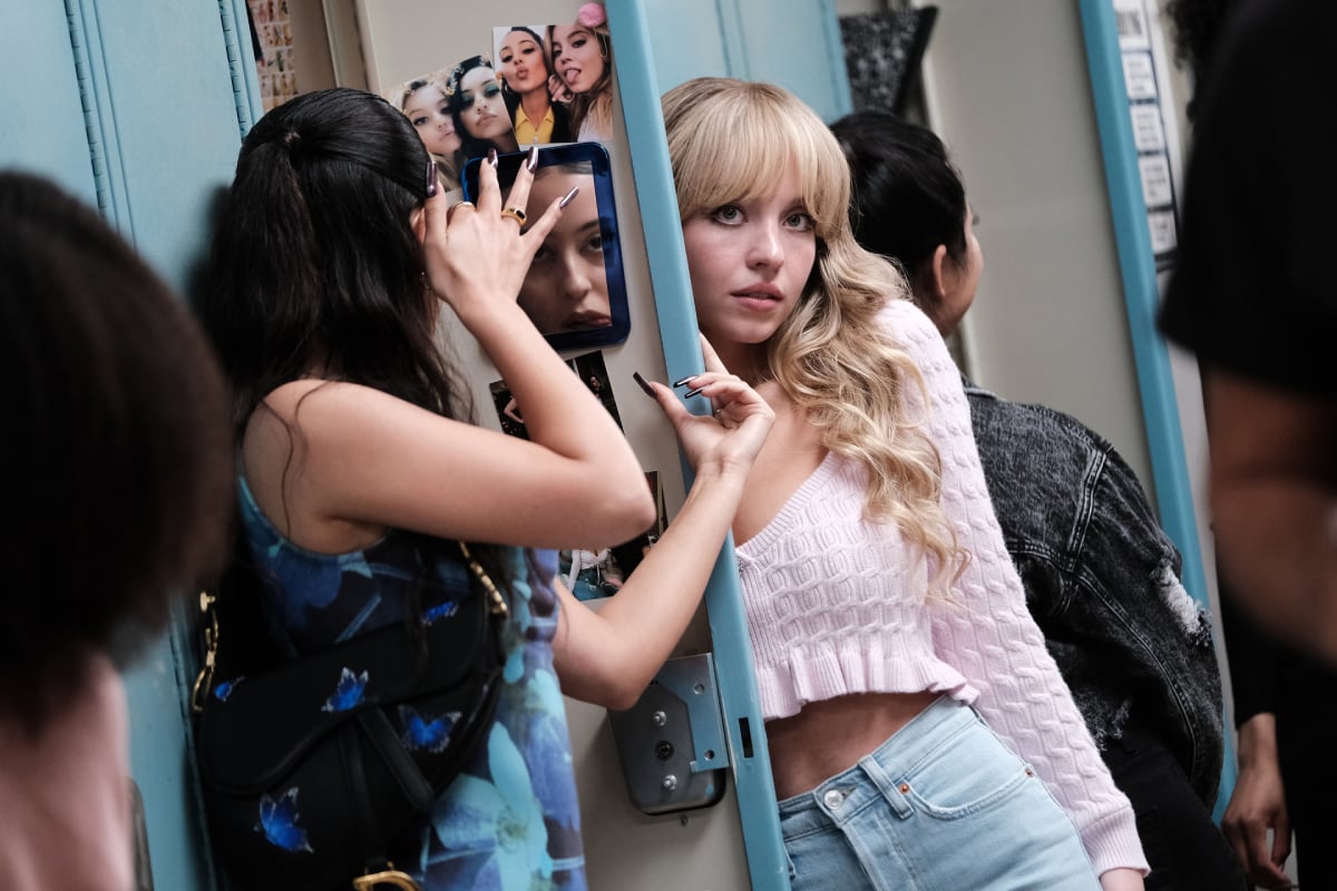 Alexa Demie as Maddy and Sydney Sweeney in Euphoria Season 2. Cassie has bangs and her hair is curly. Maddy is looking in the mirror in her locker.