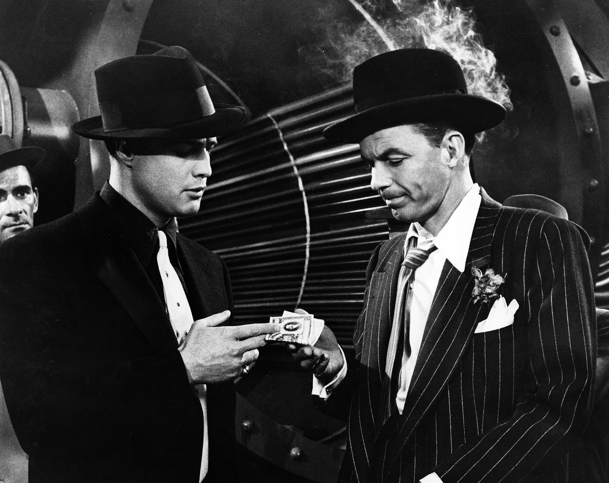 A black and white photo of Marlon Brando handing Frank Sinatra money in 'Guys and Dolls.'