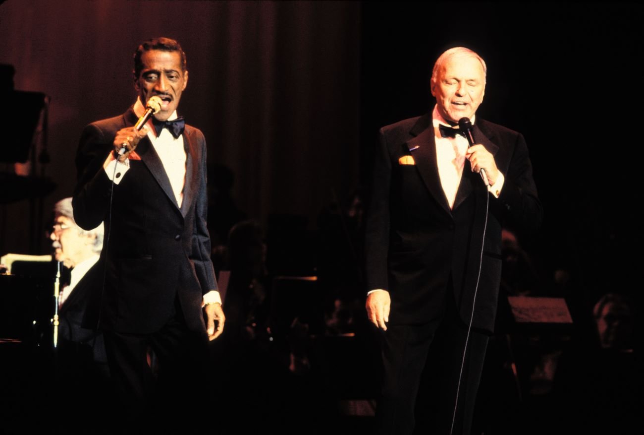 Frank Sinatra and Sammy Davis Jr. wear tuxedos and sing into microphones.
