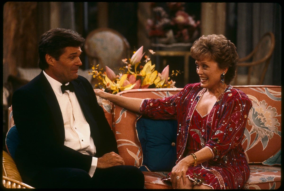 'The Golden Girls' actor Fred Willard in a tuxedo and Rue McClanahan in a burgundy dress; sit in the living room.