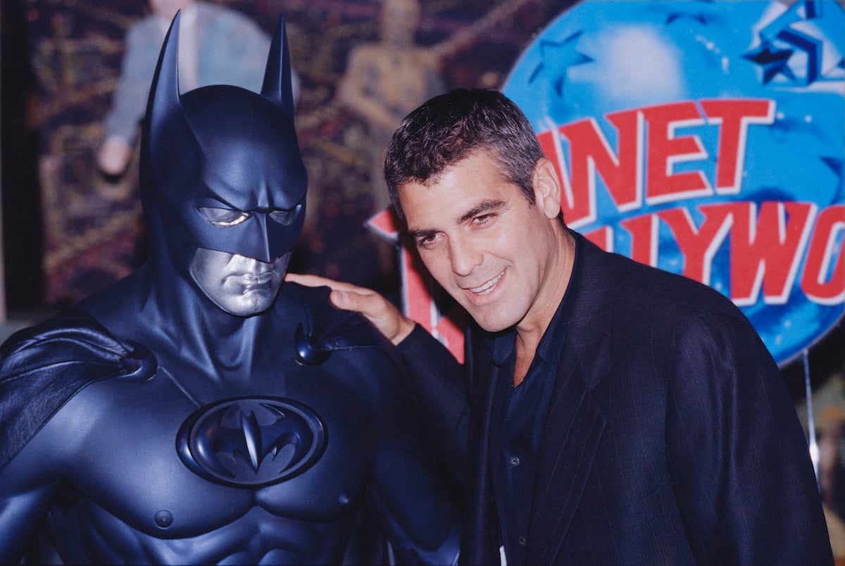 George Clooney wears black and smile while posing with a model of Batman