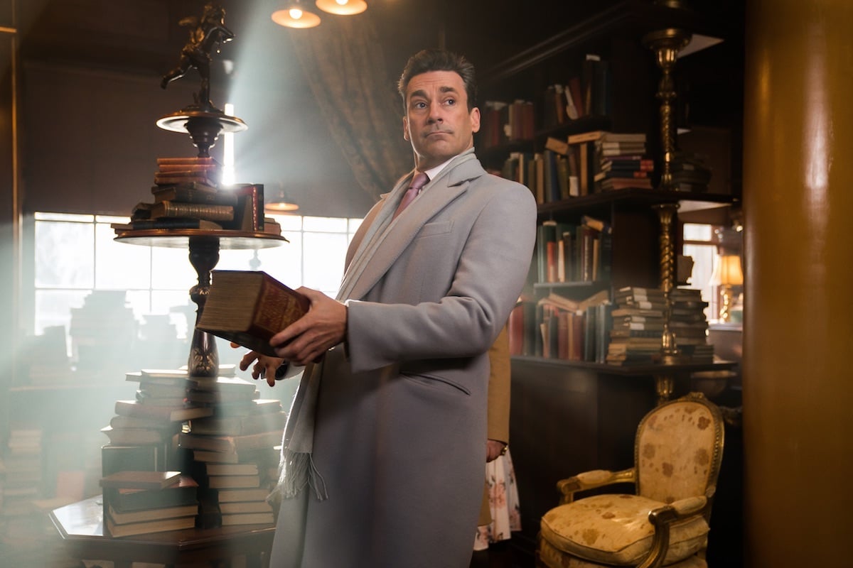 'Good Omens' cast member Jon Hamm holding a large, old book in an episode of the Prime Video series 