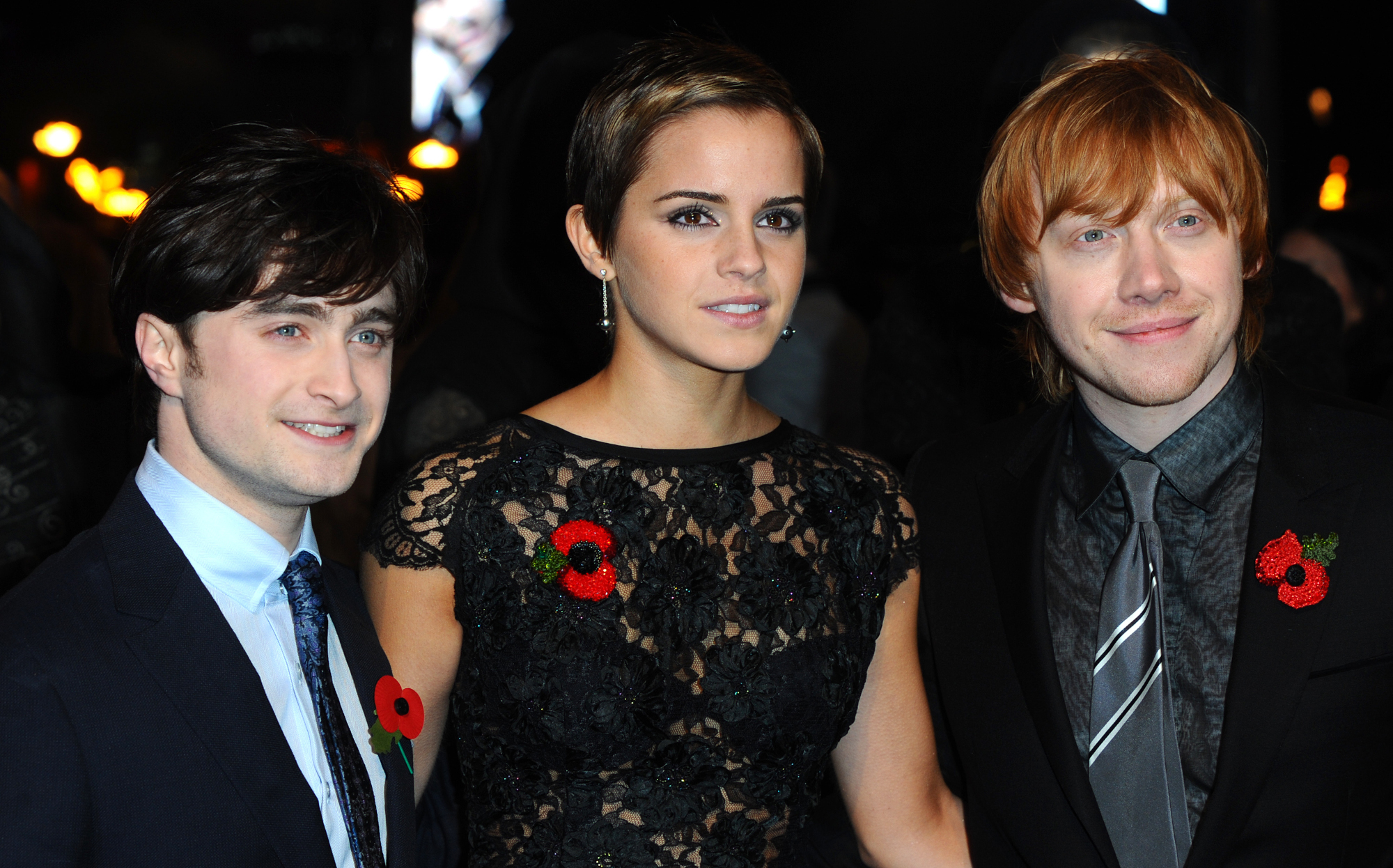 'Harry Potter' cast members Daniel Radcliffe, Emma Watson, and Rupert Grint. They're standing next to one another. Radcliffe and Grint are wearing black suits, and Watson is wearing a black dress.