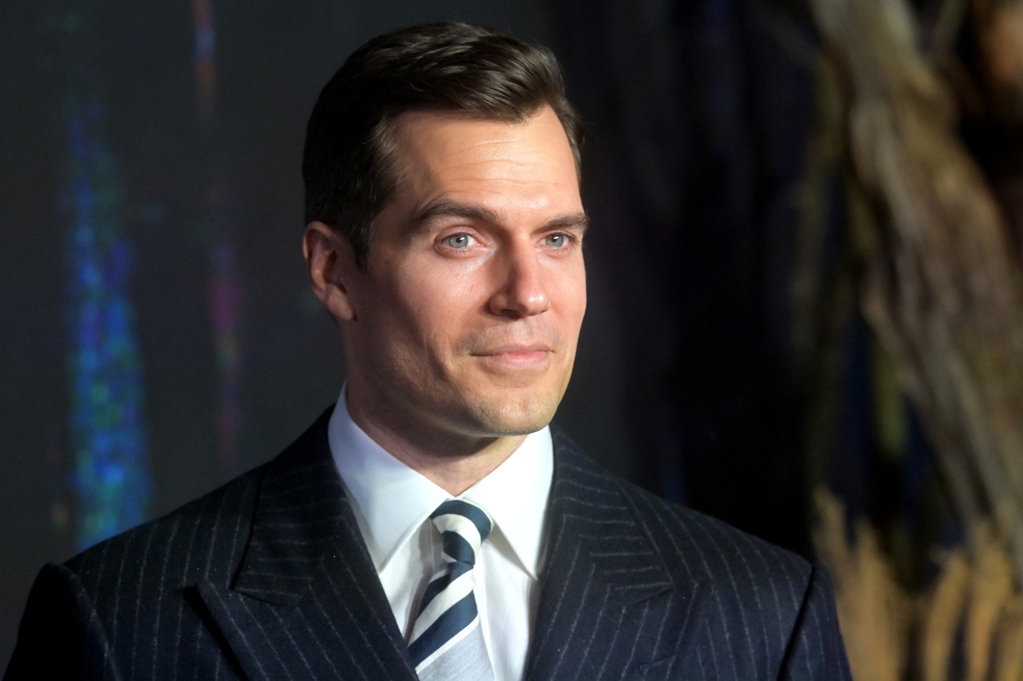 'The Witcher' star Henry Cavill on the red carpet for season 2. His brown hair is slicked back, and he's wearing a white shirt, black jacket, and black and white tie.