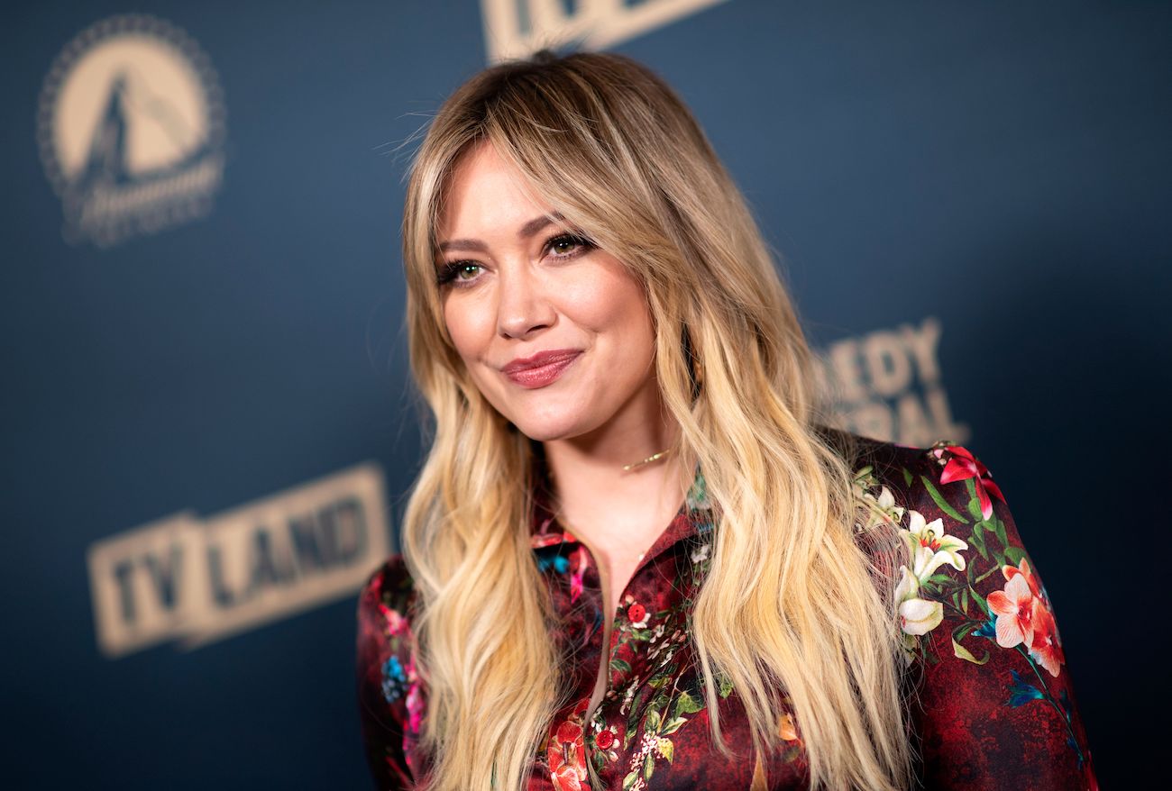 Hilary Duff with long blonde hair, standing in front of a blue background