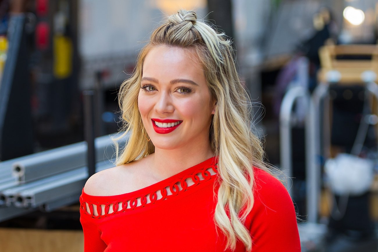 Hilary Duff wearing a red off-shoulder top, smiling into camera