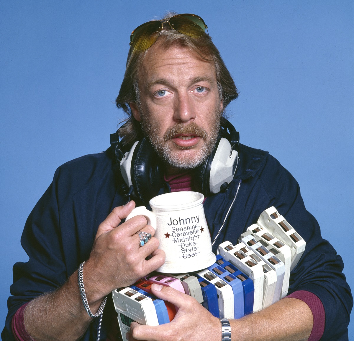 'WKRP in Cincinnati' star Howard Hesseman wearing sunglasses and headphones, and carrying tapes and a coffee mug.