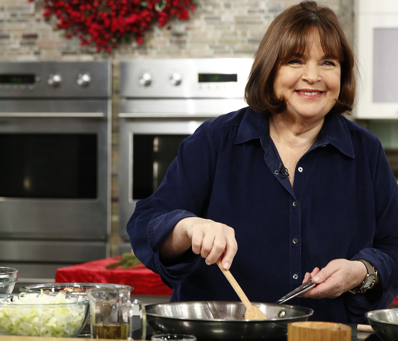 Ina Garten stirs with a wooden spoon wearing a blue button-down shirt wearing a