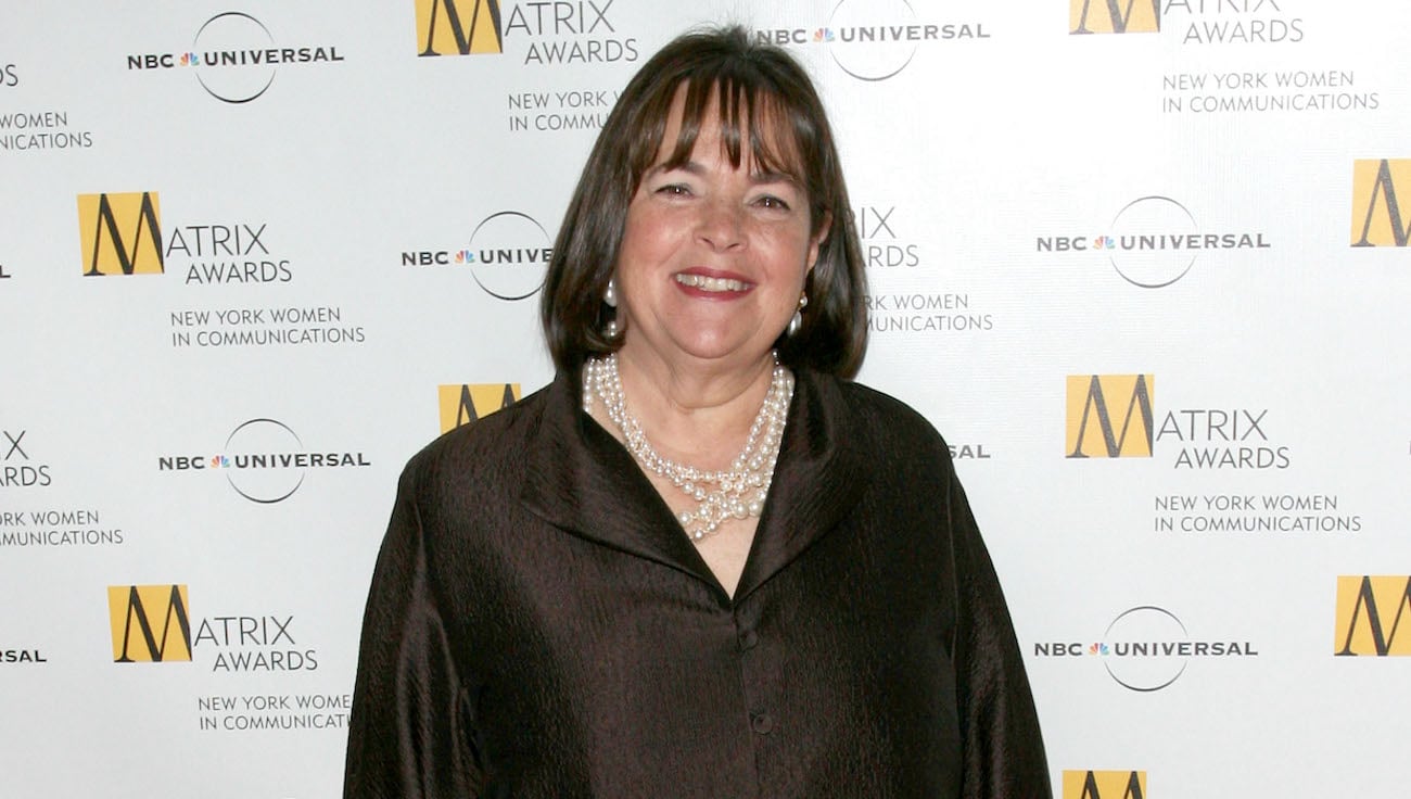 Ina Garten smiles posing for photographers wearing a brown shirt and pearl necklace
