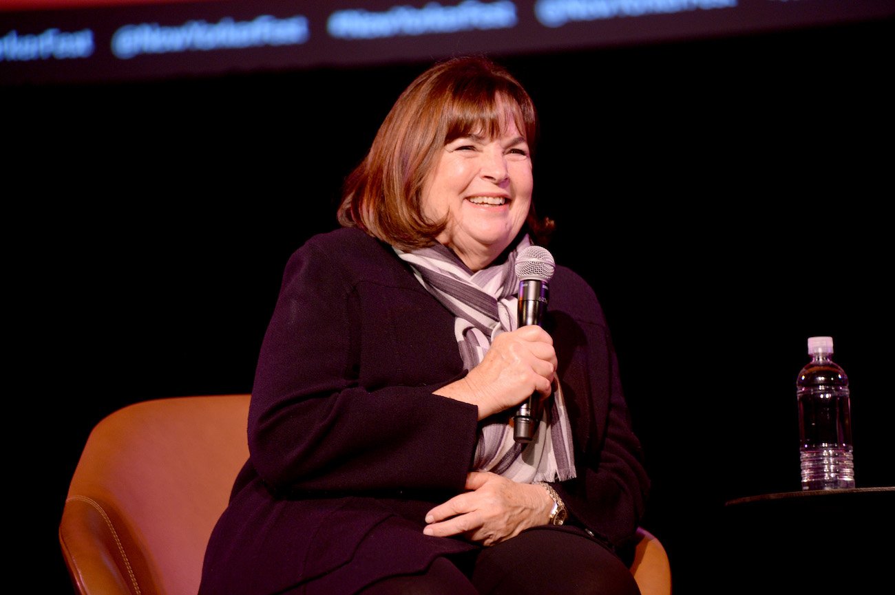 Ina Garten smiles holding a microphone and sitting in a chair