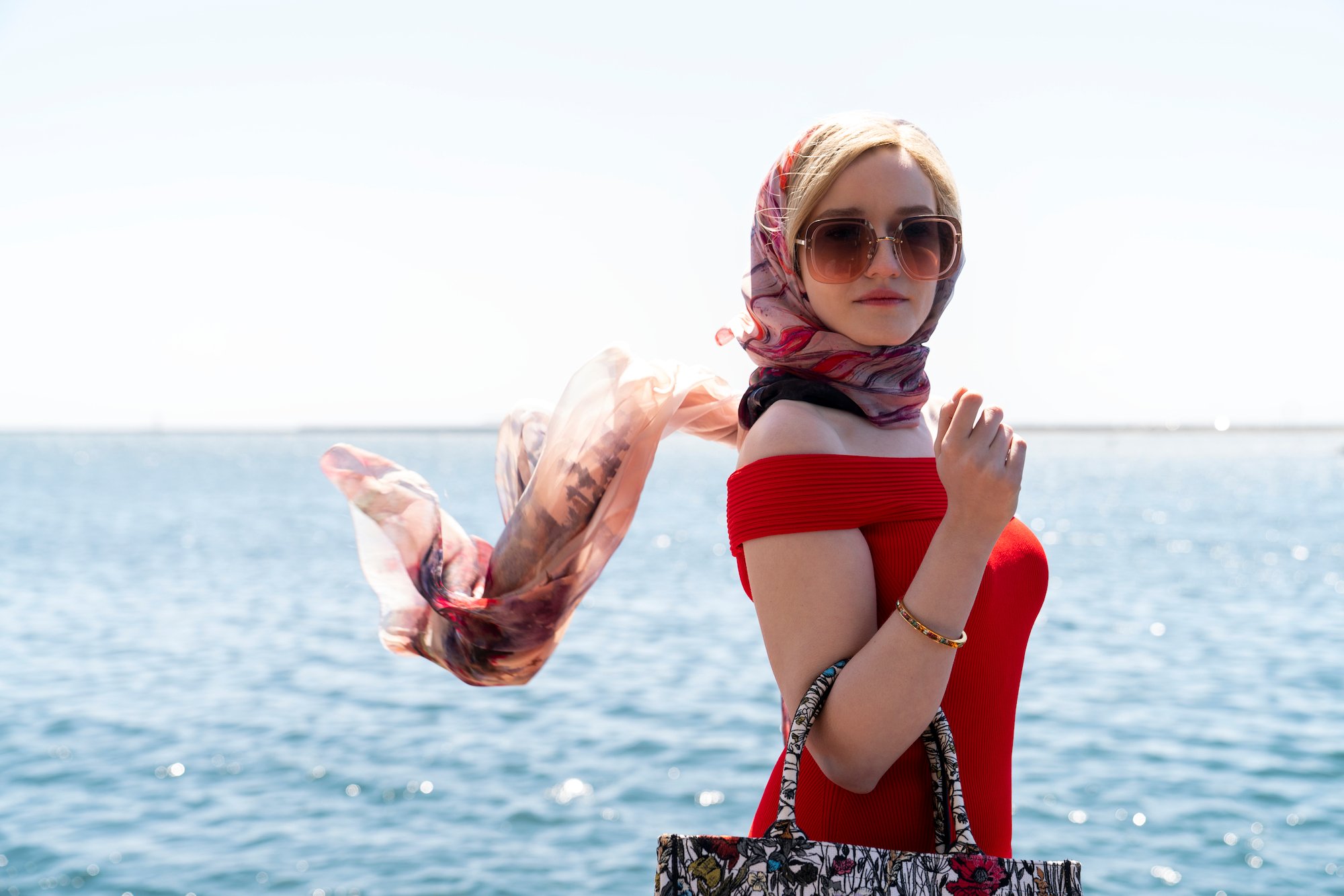 Julia Garner in a red dress in front of a body of water in a production still from Shonda Rhimes new series 'Inventing Anna.'