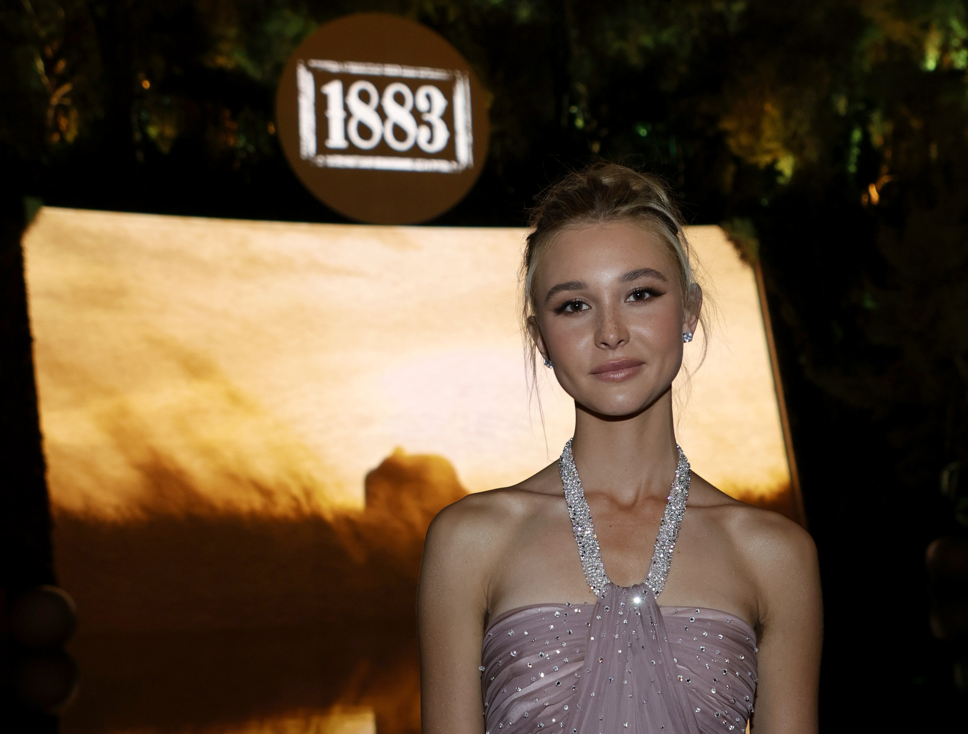 Isabel May attends the after party for the world premiere of 1883 at SW Steakhouse at Wynn Las Vegas. May wears a lavender dress and her hair is in an updo.