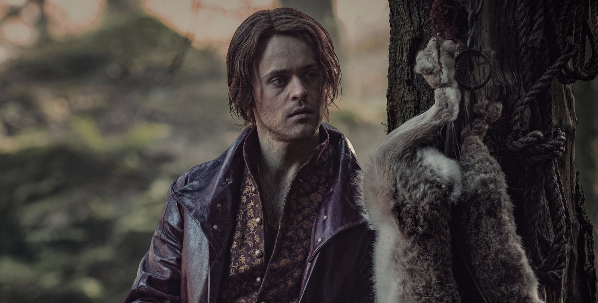 Jaskier in 'The Witcher' Season 2 Episode 7 in the forest next to animal nailed to a tree.
