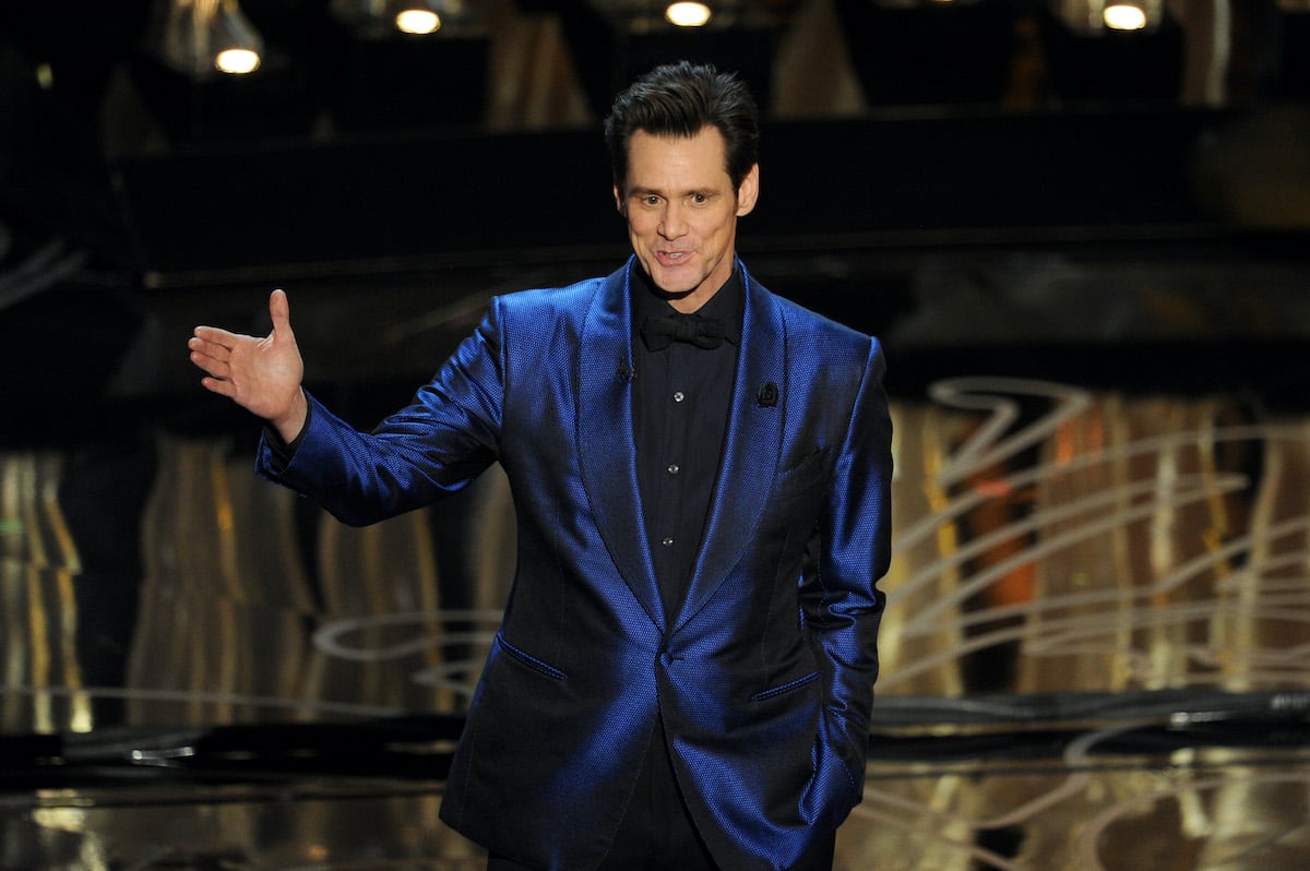 Jim Carrey wears a suit with a blue jacket onstage while smiling at the Oscars