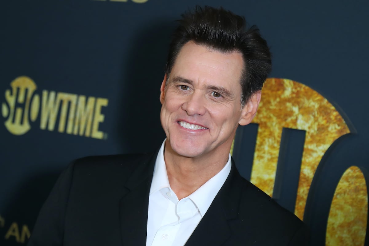 Jim Carrey wears a black jacket and smiles in front of the Showtime logo