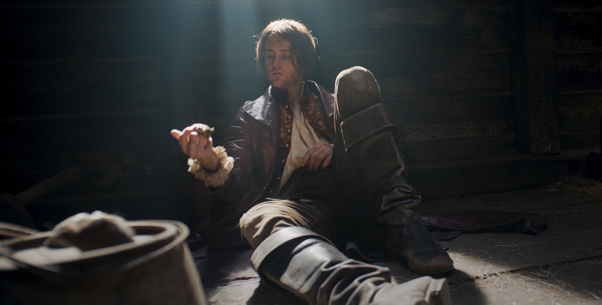 Joey Batey as Jaskier in 'The Witcher' Season 2 sitting in a cell holding a mouse.