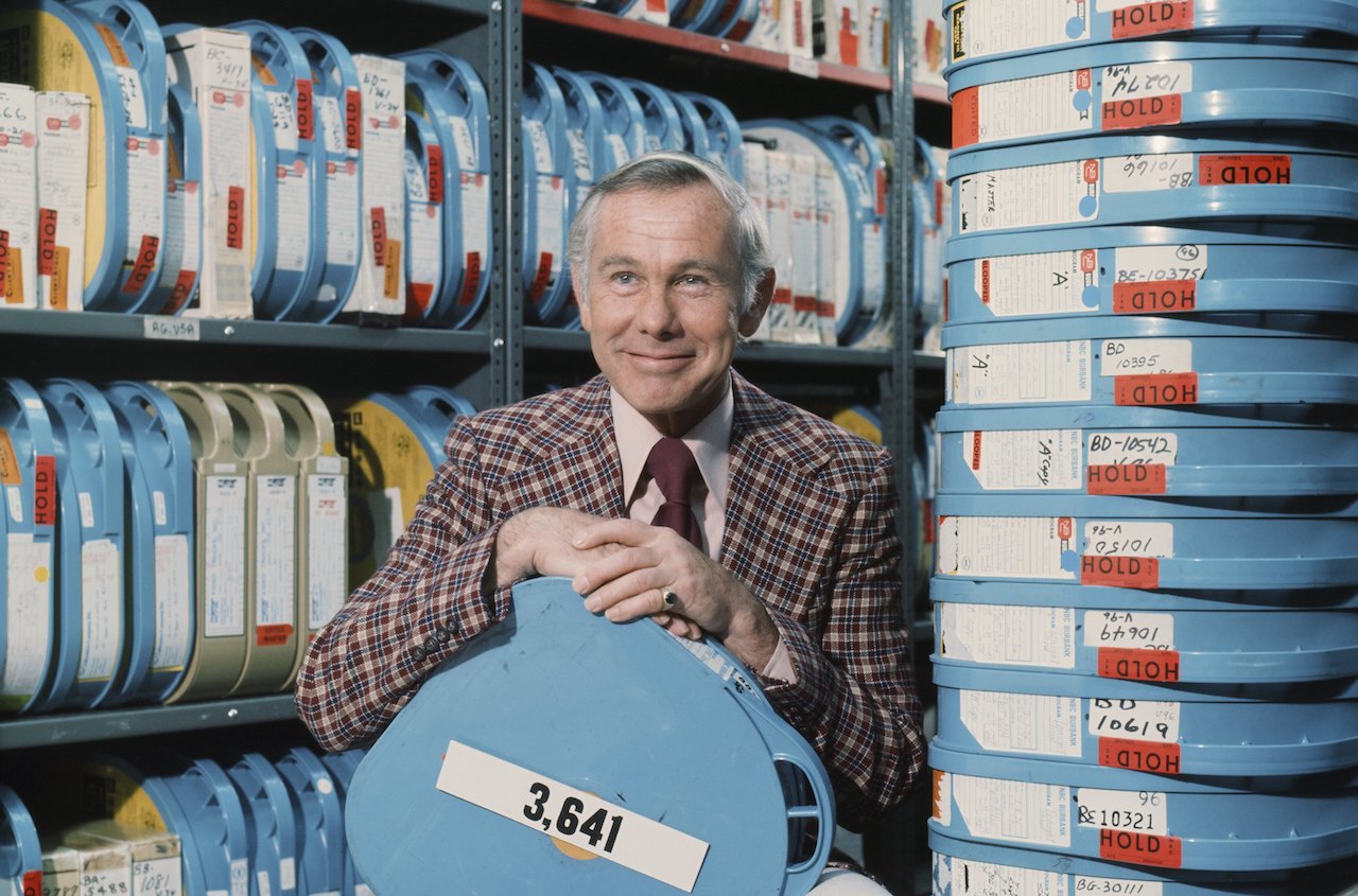 Johnny Carson in a plaid jacket, holding a film tape c. 1976