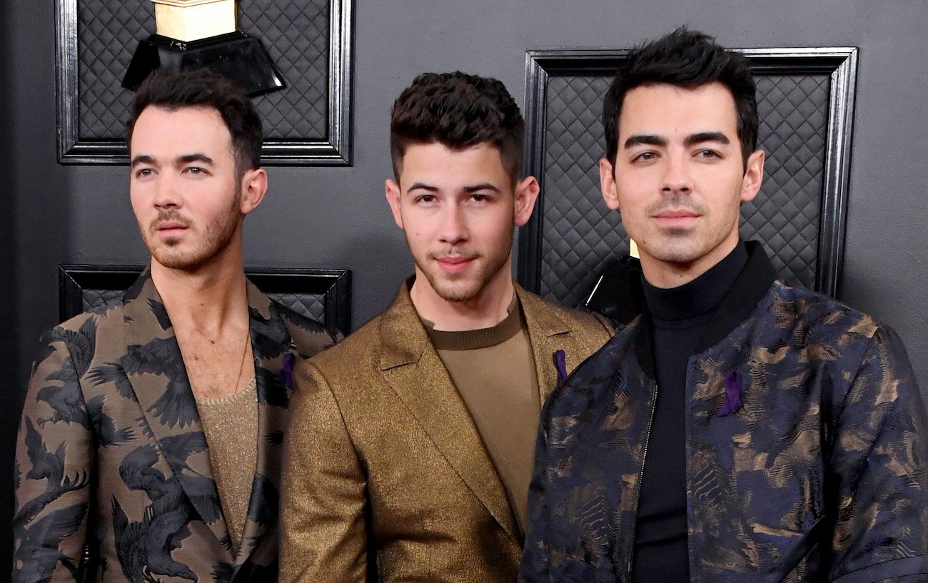 Kevin, Nick, and Joe Jonas looking in various directions in front of a gray background