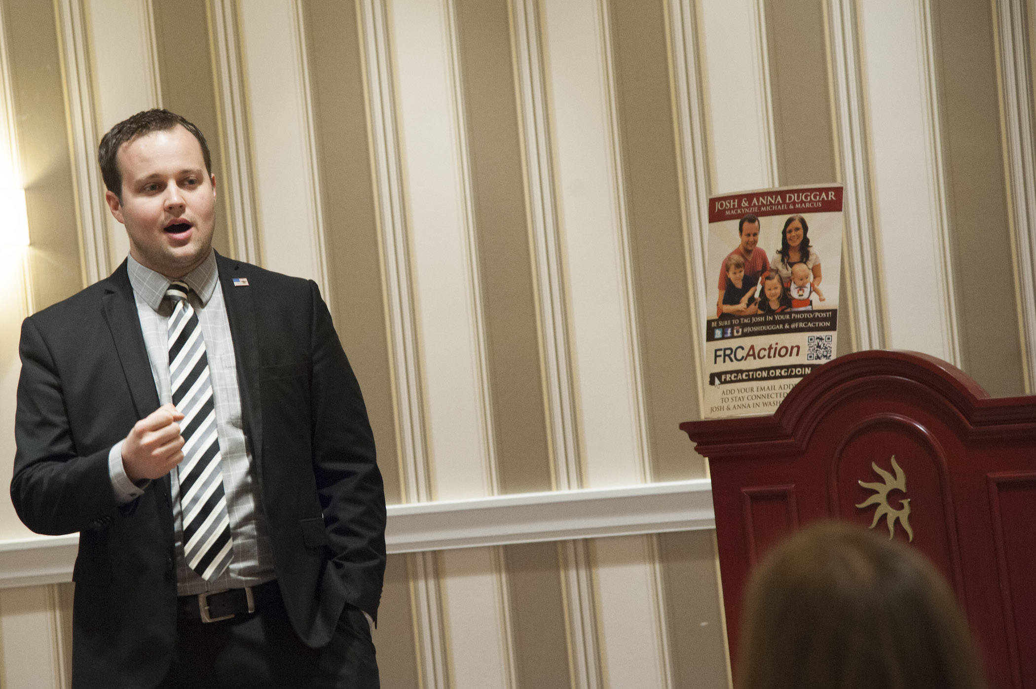 Josh Duggar of the Duggar family speaking at a conference in a suit