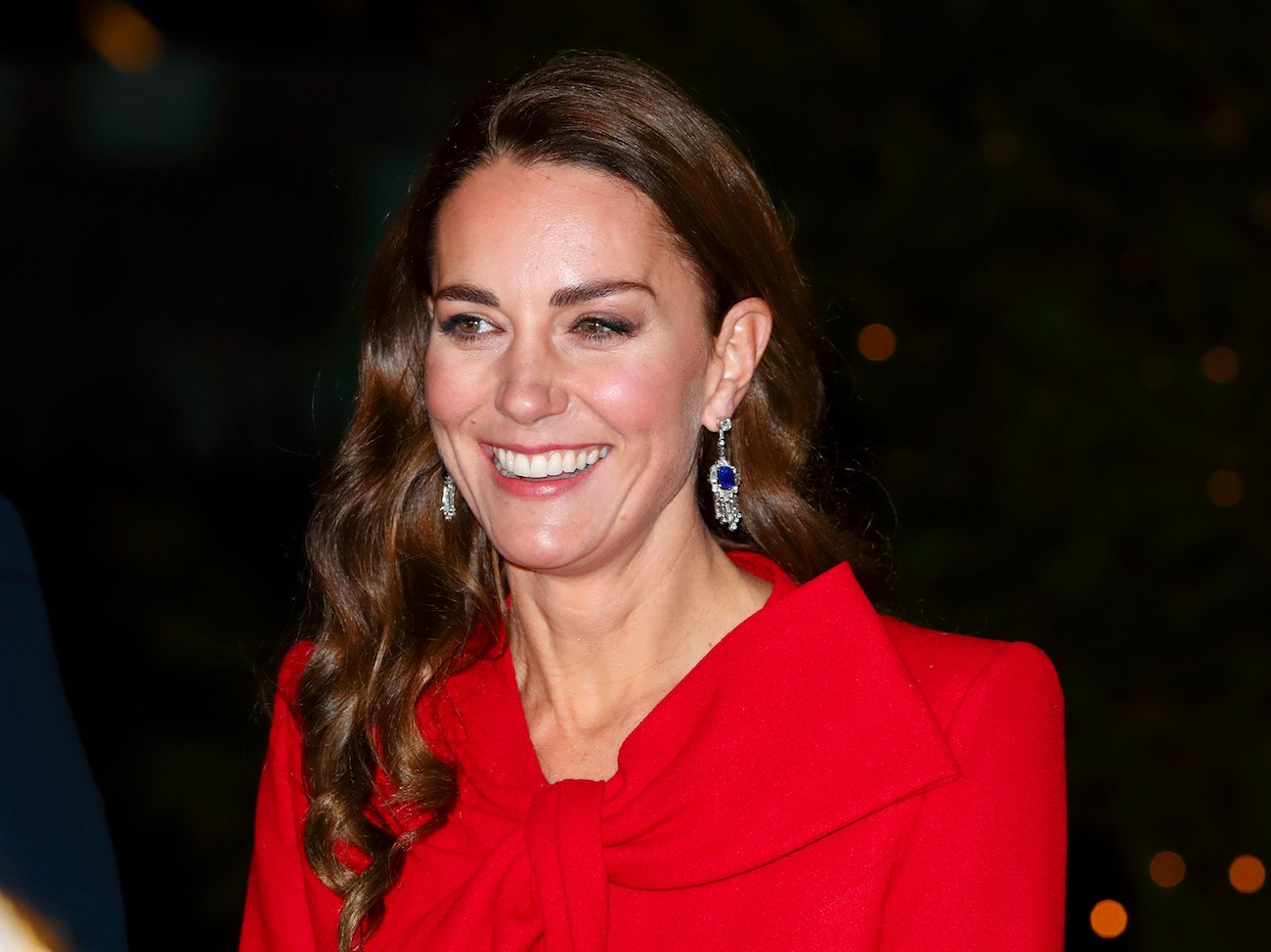 Kate Middleton smiles wearing a red coat as she arrives at 'Together at Christmas' carol TV special
