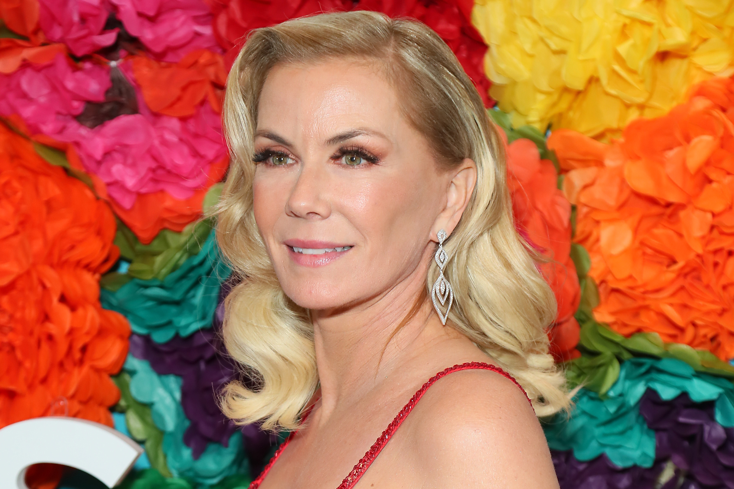 'The Bold and the Beautiful' actor Katherine Kelly Lang wearing a red dress and posing in front of a floral hedge.