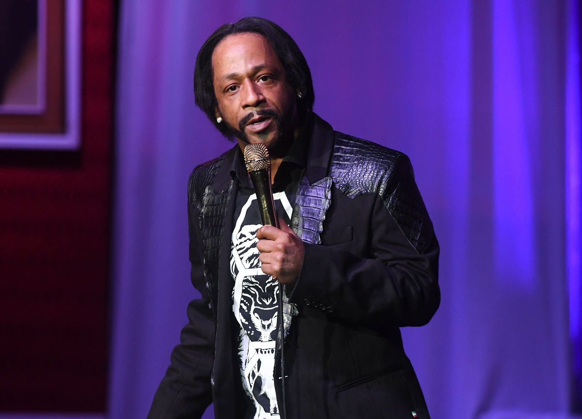 Katt Williams wearing a black jacket while holding a microphone.