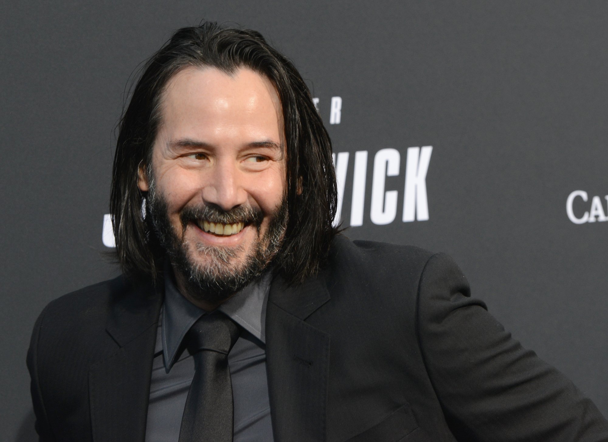 Keanu Reeves smiling in front of step and repeat