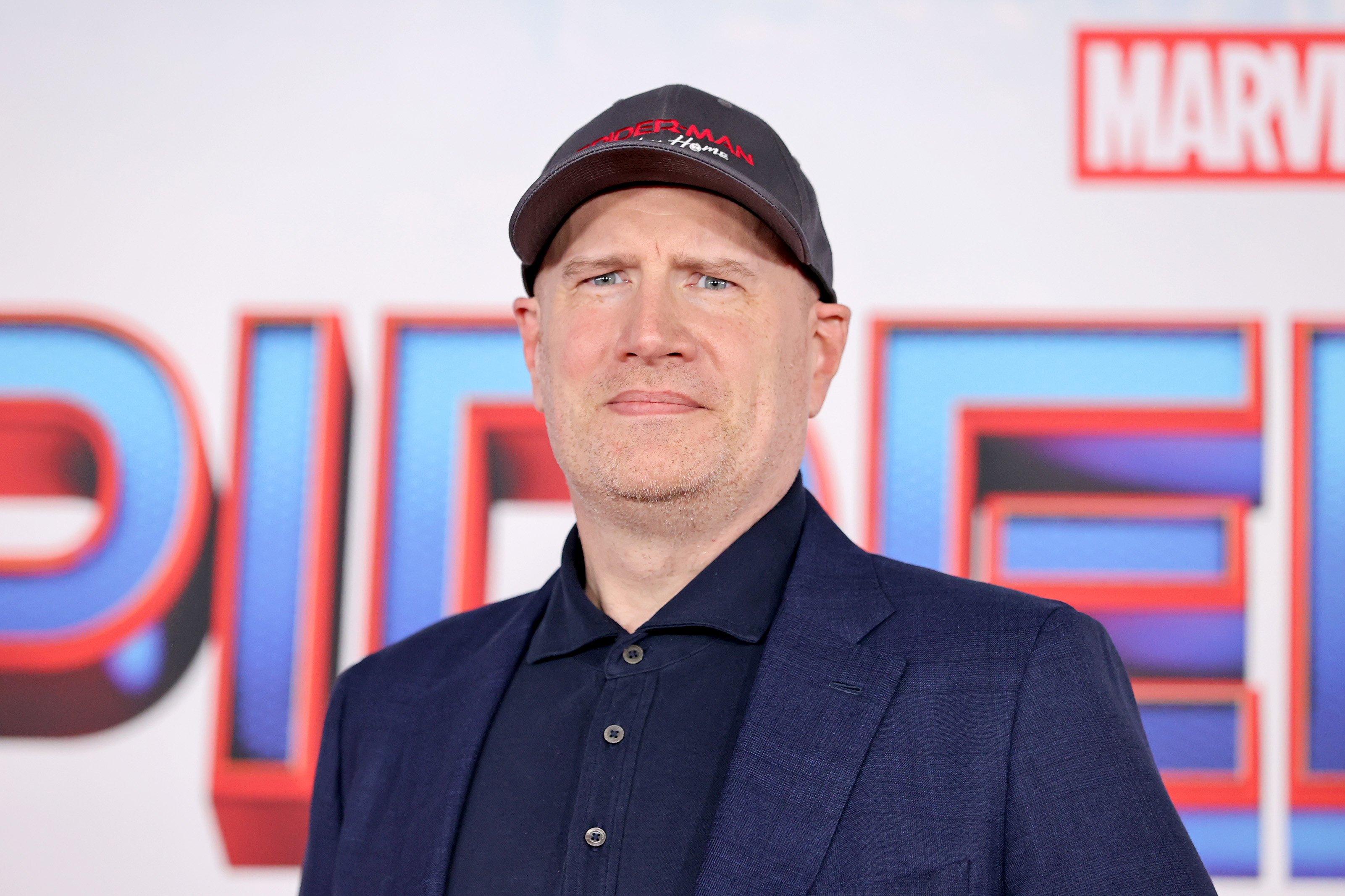 Marvel Studios President Kevin Feige wears a 'Spider-Man: No Way Home' baseball cap and a blue suit jacket over a blue button-up shirt.