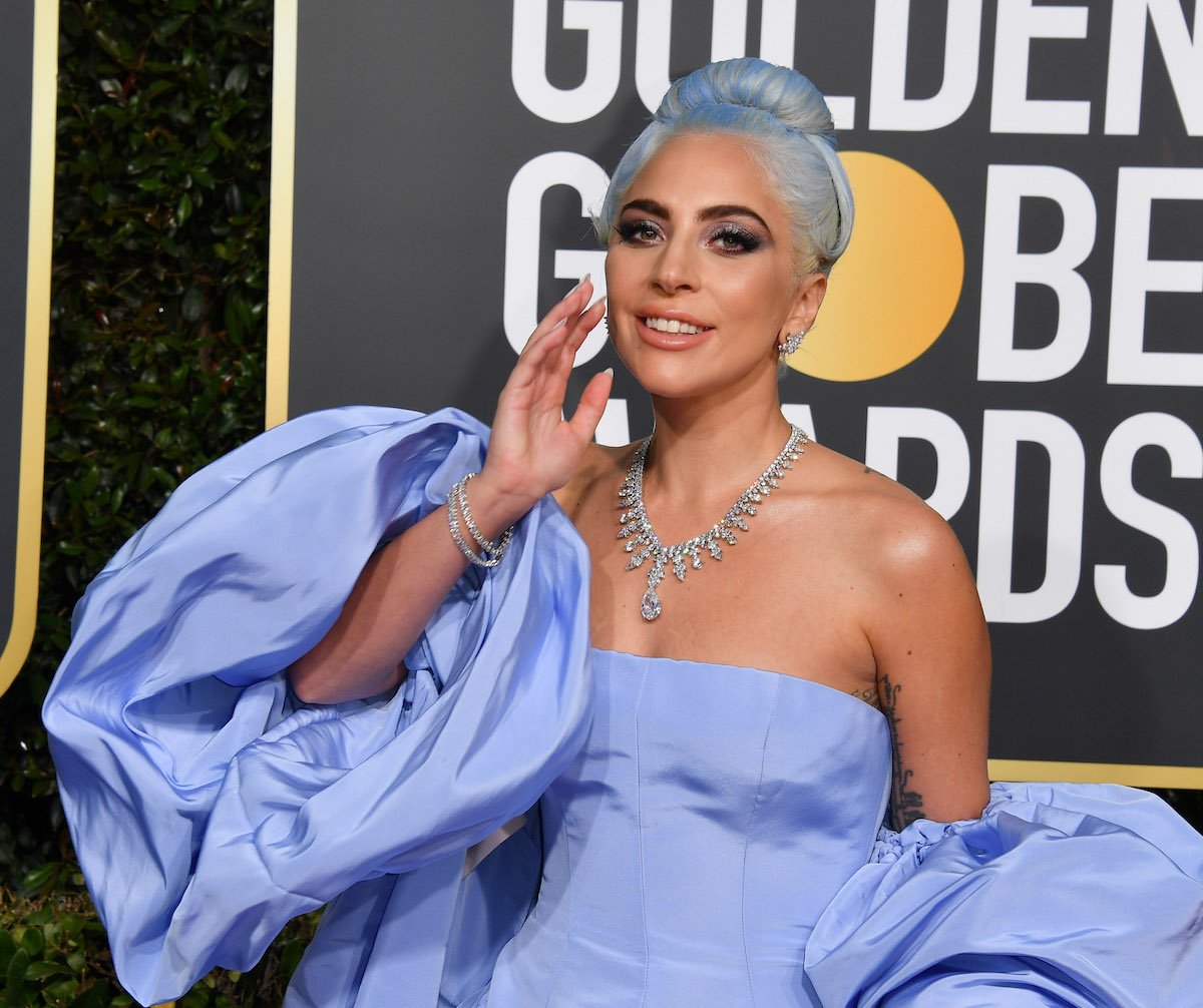 Lady Gaga wears a lavender dress and jewelry as she smiles on the Golden Globes red carpet
