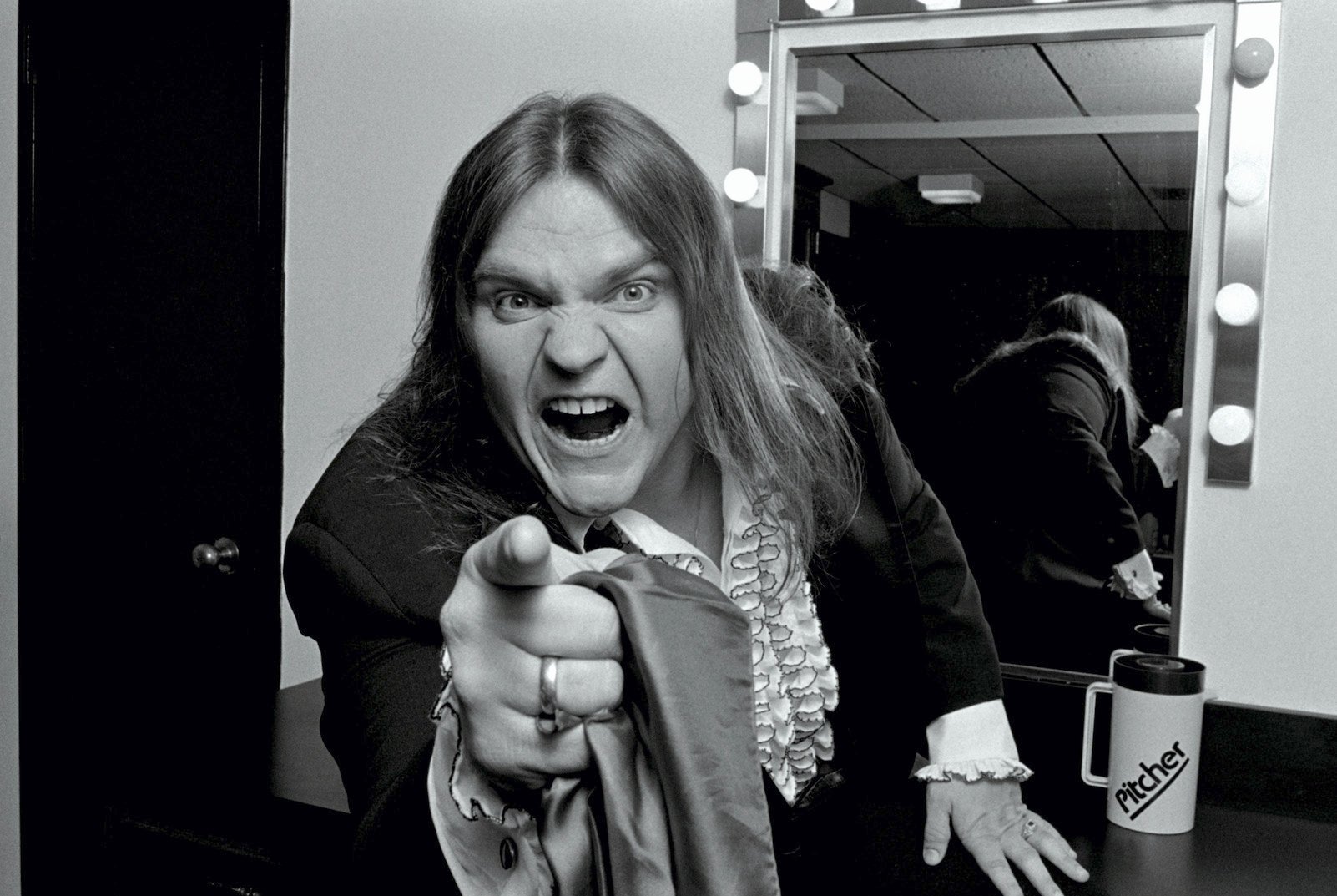 A black and white photo of Meat Loaf backstage in 1981 pointing his finger at the camera aggressively