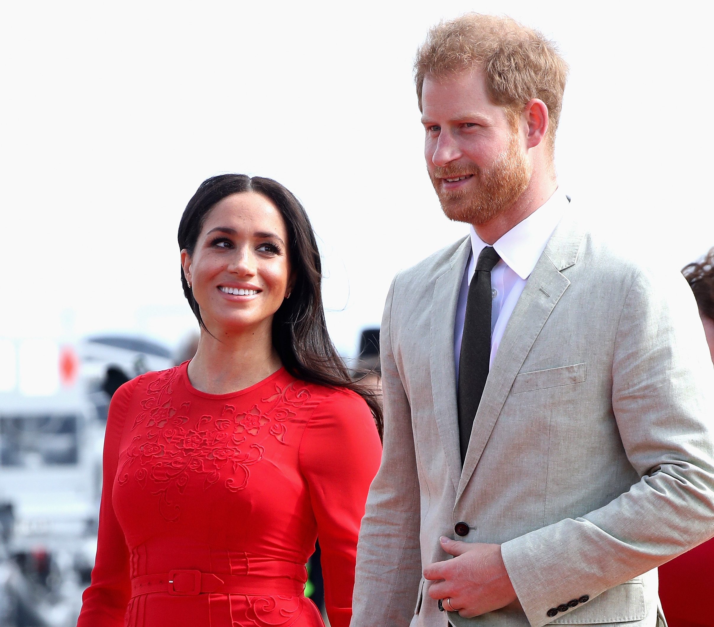 Meghan Markle donning a red dress as she smiles at Prince Harry upon arrival in Tonga