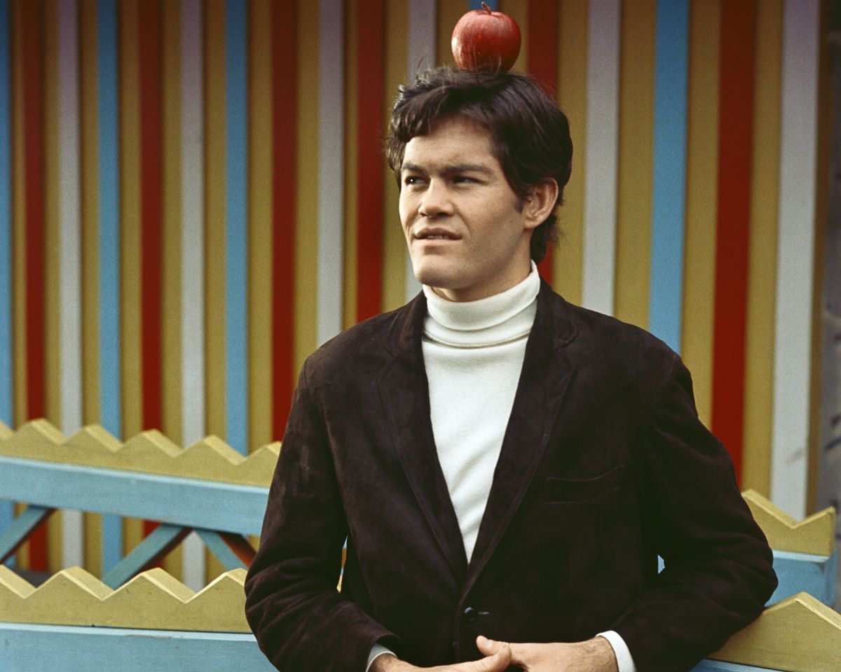 Micky Dolenz in a brown jacket with an apple on top of his head
