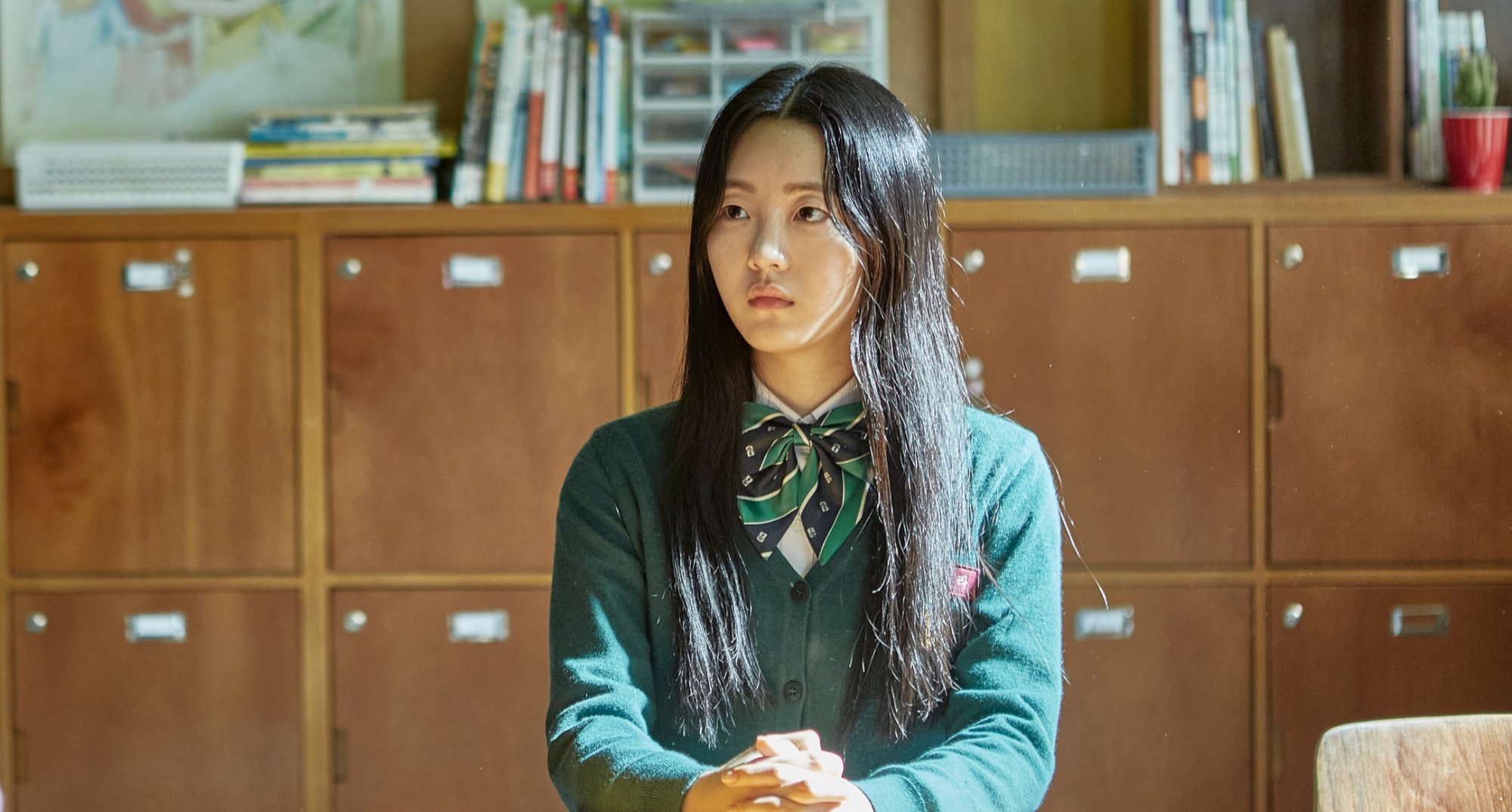 Nam-ra character in 'All of Us Are Dead' and season 2 sitting at desk wearing uniform.