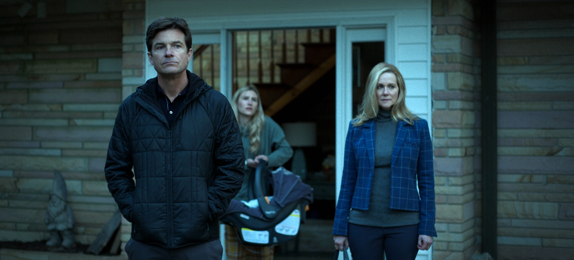 Ozark Season 4 stars Jason Bateman, Sofia Hublitz, and Laura Linney stand outside the Byrde's house in a production still.