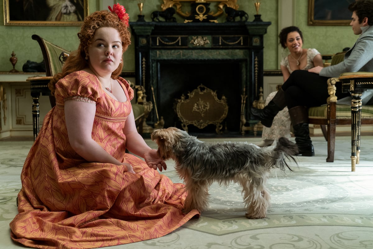 Nicola Coughlan as Penelope Featherington, wearing an orange dress and kneeling next to a dog, in 'Bridgerton' Season 1