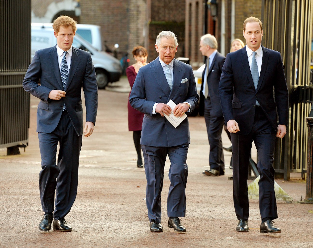 Prince Harry, Prince Charles, and Prince William wearing suits while walking next to each other