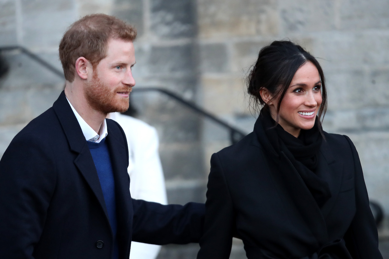 Prince Harry and Meghan Markle wearing dark outfits and looking off-camera to the right