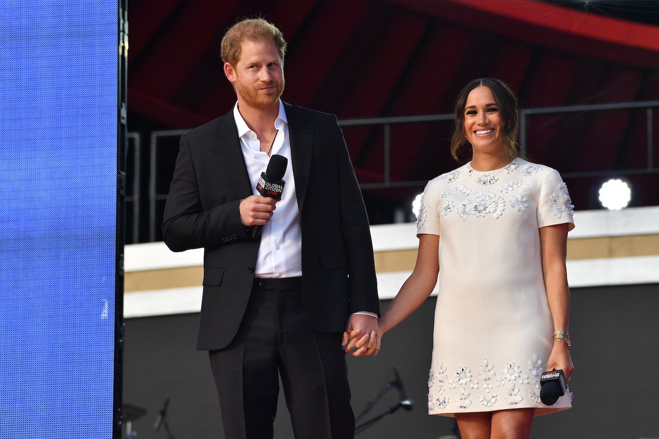 Prince Harry and Meghan Markle hold hands as they stand onstage