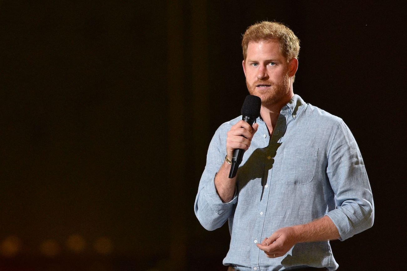 Prince Harry speaks into a microphone wearing a blue button-down shirt