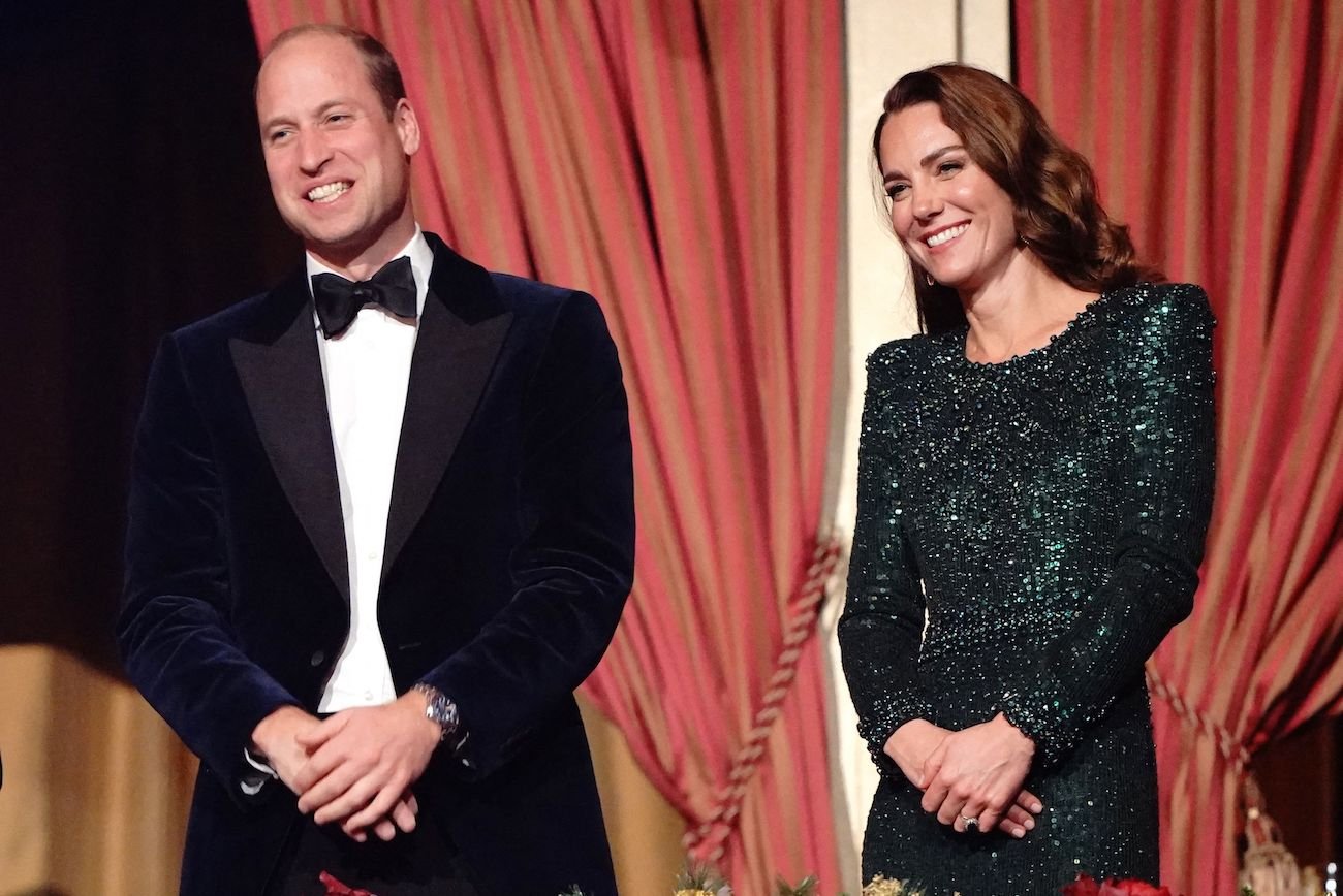 Prince William smiles in a tuxedo as he stands next to Kate Middleton in a green gown