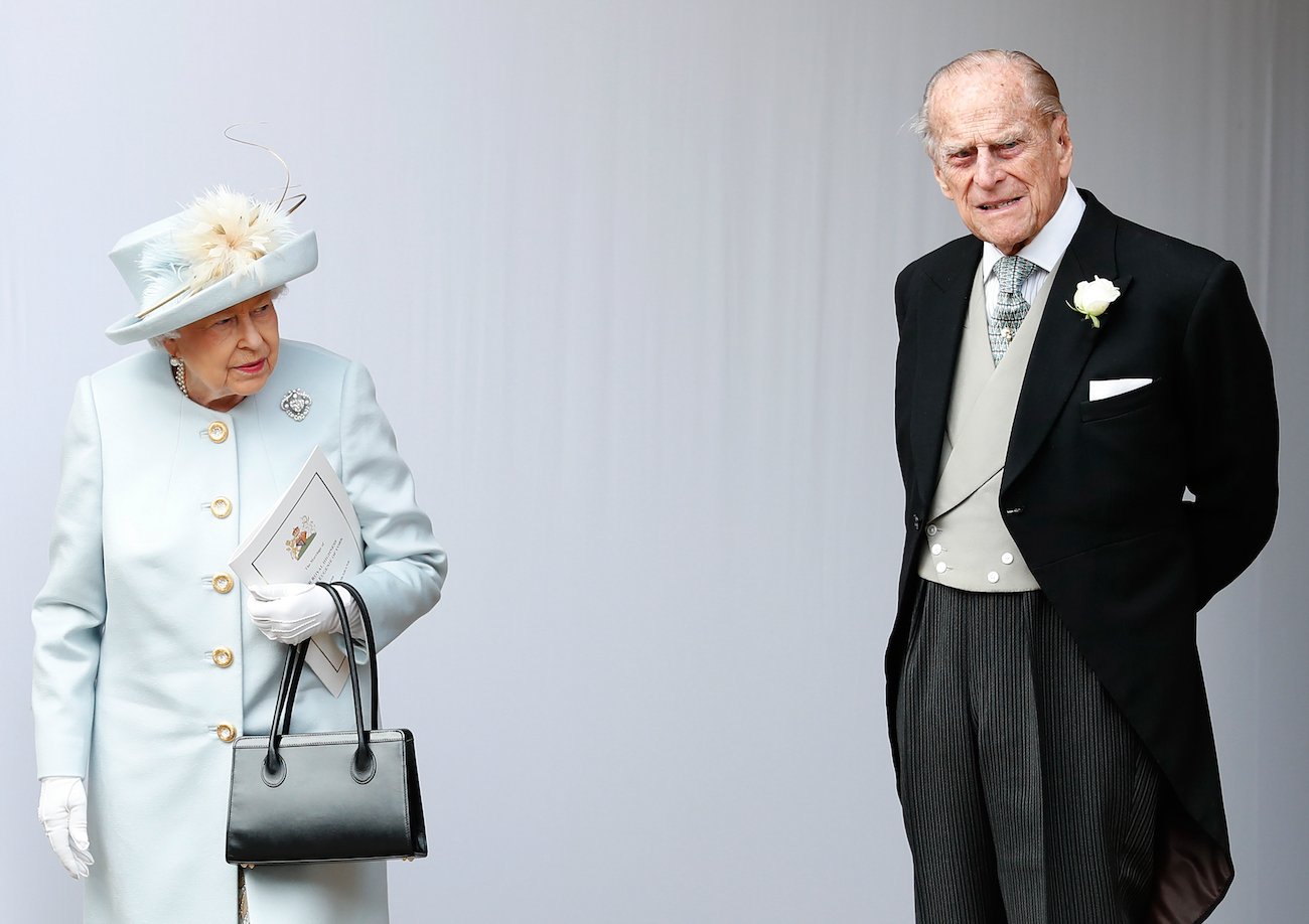 Queen Elizabeth II wears a blue coat and hat as she stands near Prince Philip