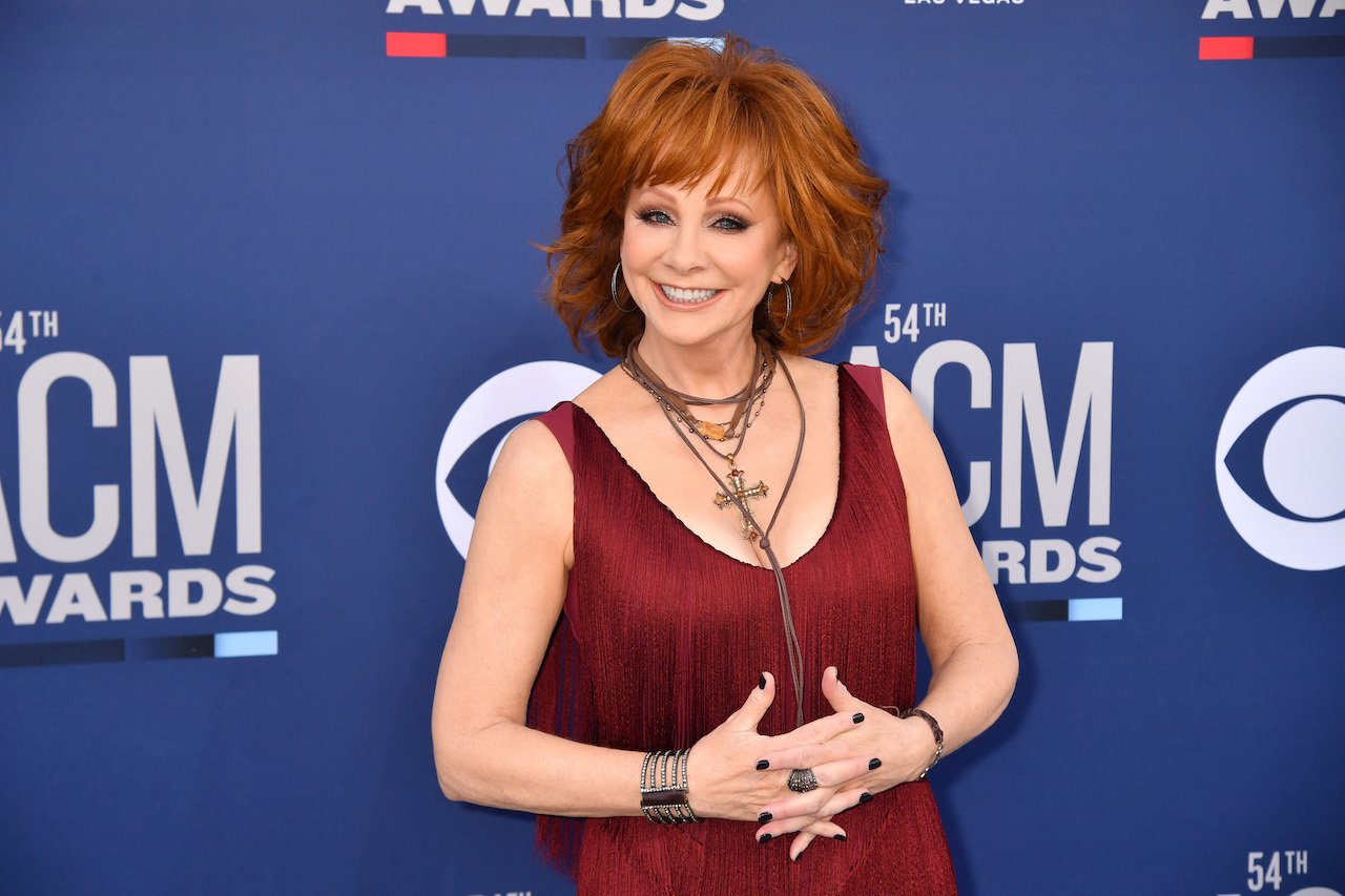 Reba McEntire in a red sleeveless dress, standing with her hands interlocked in front of her