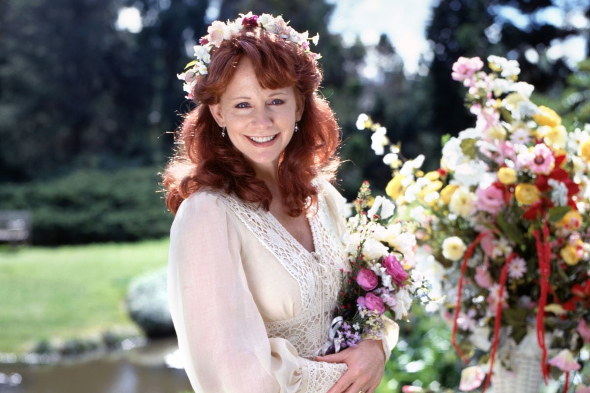 Reba McEntire poses in a white dress holding flowers for a made-for-TV movi