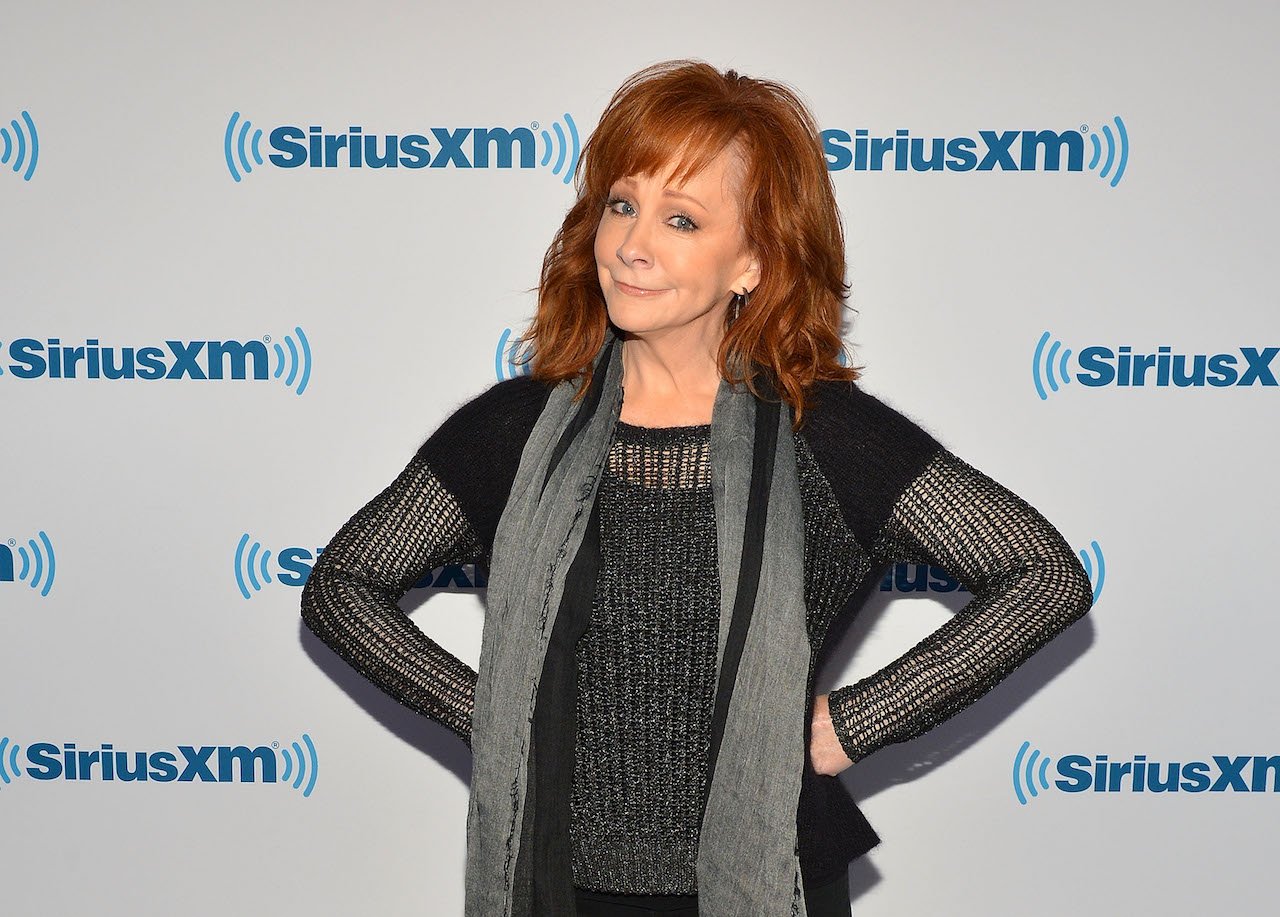 Reba McEntire stands with her hands on her hips, dressed in a black shirt