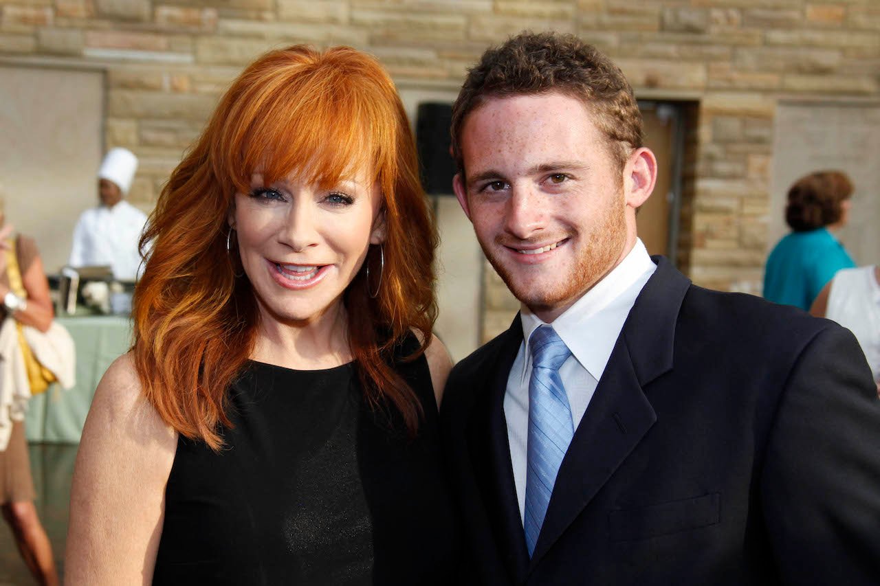 (lr) Reba McEntire in a black dress, standing with her son, Shelby Blackstock, in a black coat with a blue tie